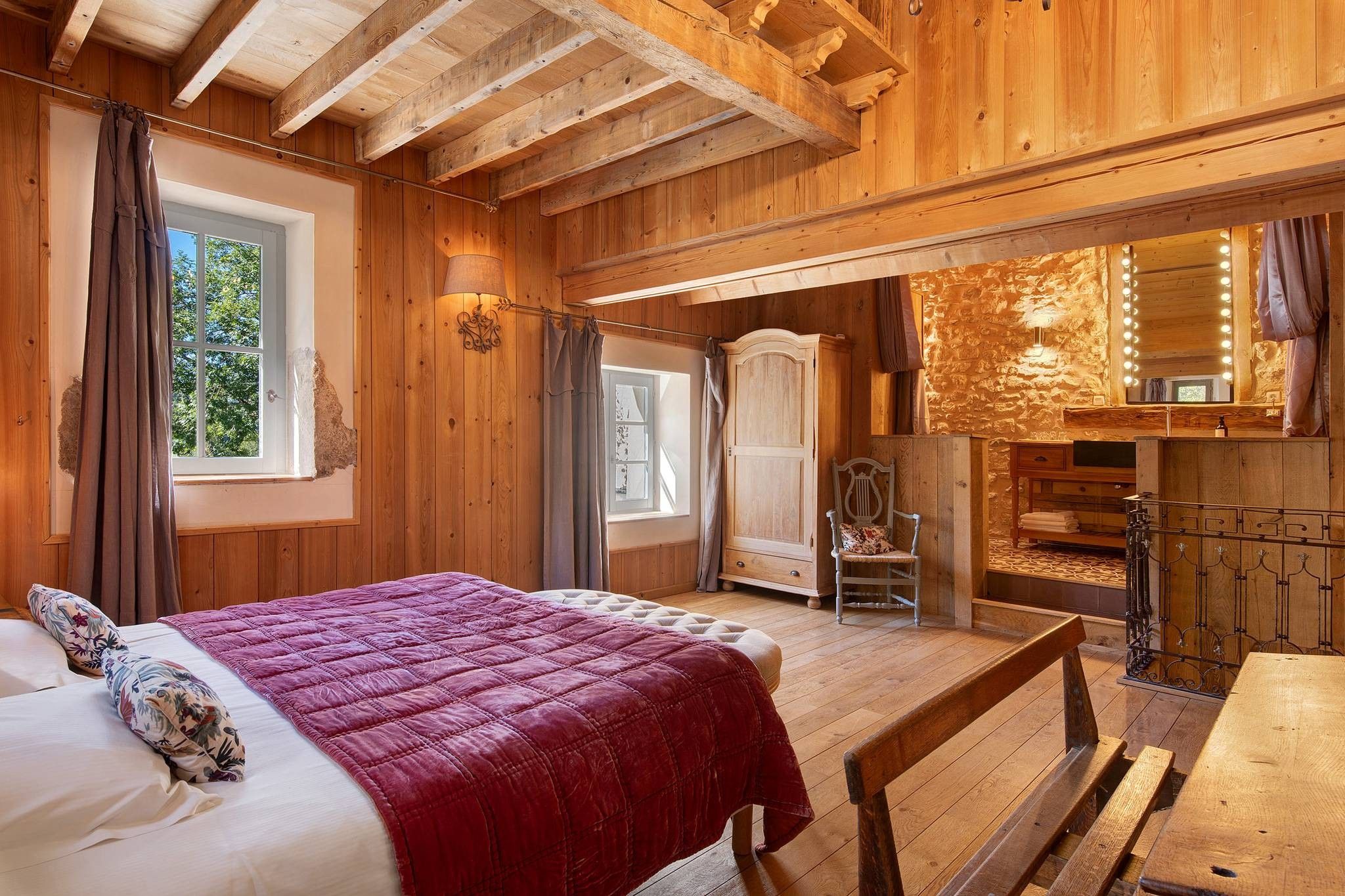 Un intérieur en bois comprenant un lit, un banc, une chaise et un petit coin cuisine.