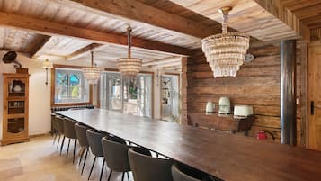Une longue table à manger en bois, avec des chaises, un lustre et un gramophone d’époque.