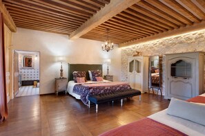 A bedroom with a wooden ceiling, a bed with a patterned bedspread, a bench, a dresser, and a mirror. - Château 'Le Chateau Des Girards' authentically renovated (Lans-en-Vercors)