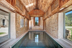 A spa area with a central pool, wooden ceiling beams, stone walls, and a view of the outdoors. - Château 'Le Chateau Des Girards' authentically renovated (Lans-en-Vercors)