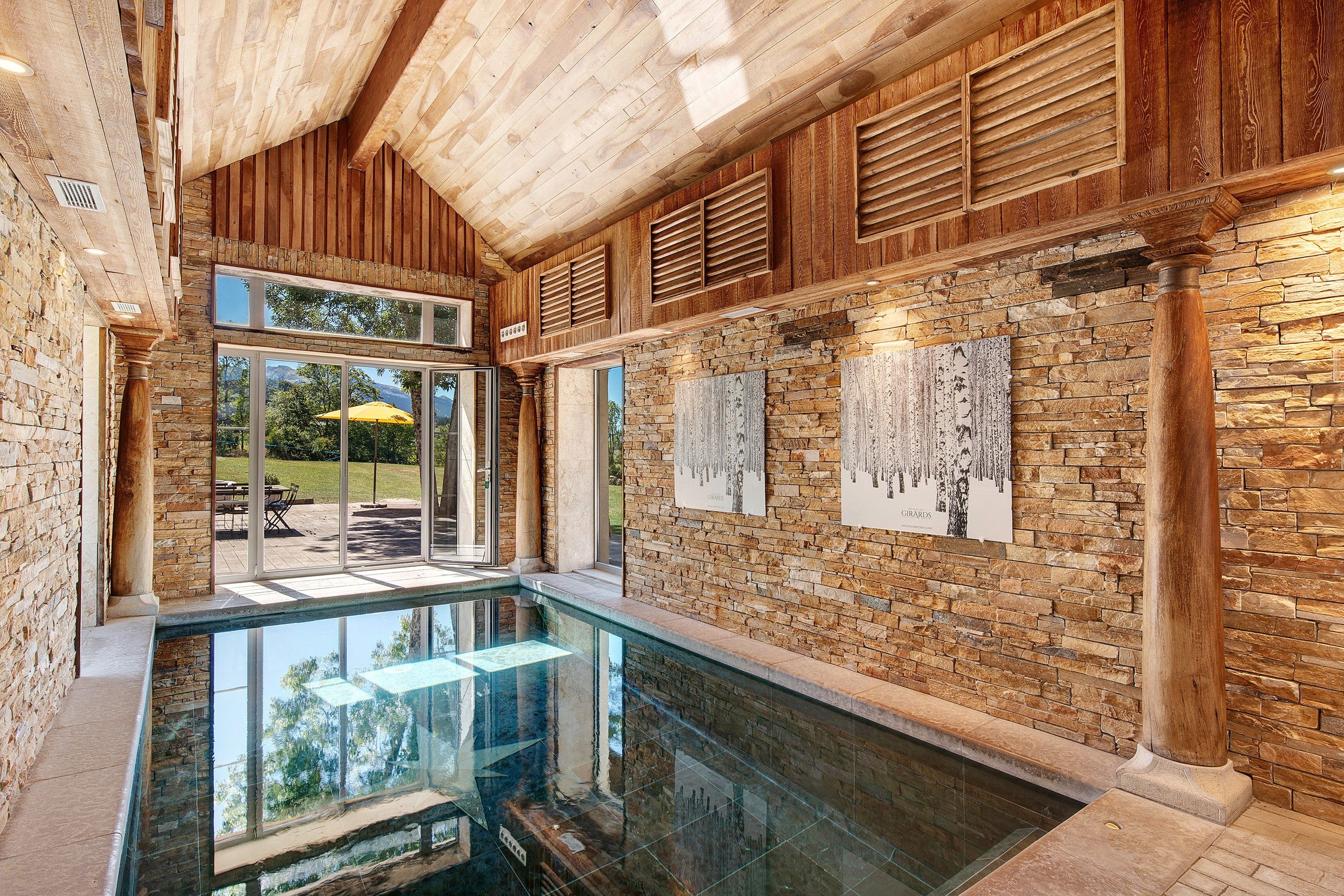 A spacious indoor pool area with a glass floor, wooden ceiling, and stone walls.