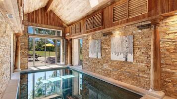 A spacious indoor pool area with a glass floor, wooden ceiling, and stone walls.