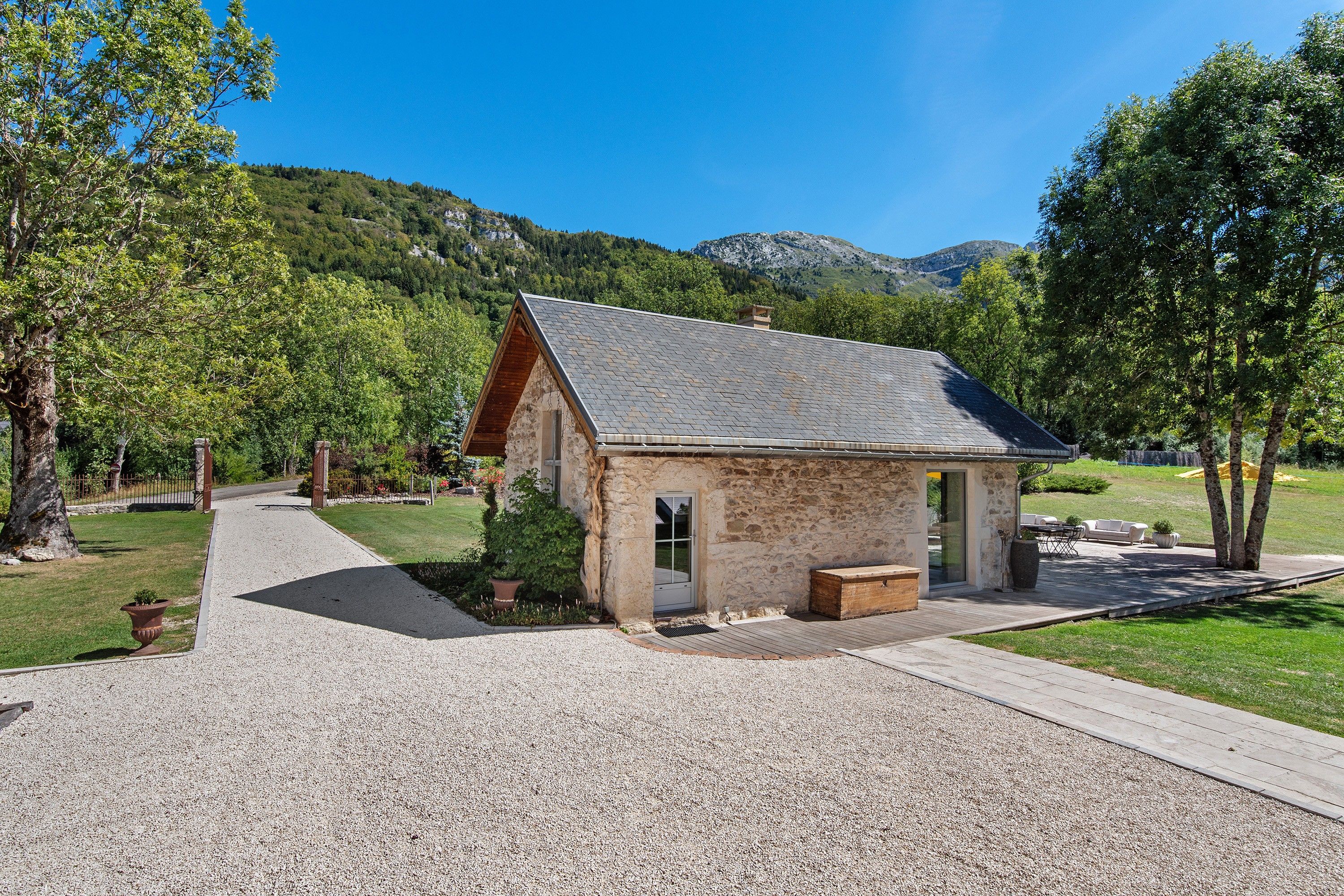 A stone building with a sloped roof, a gravel driveway, and a wooden bench.