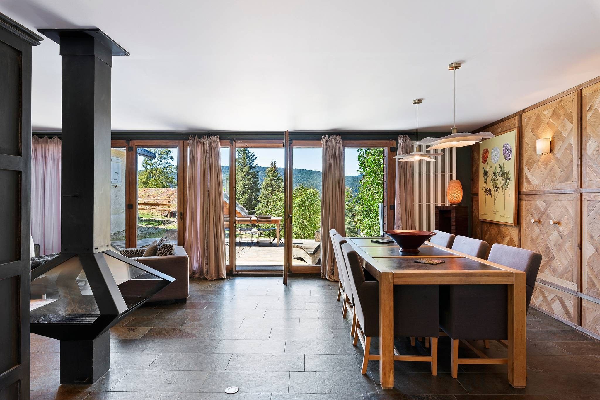 Un intérieur moderne agrémenté d’une cheminée, d’un coin repas et de grandes fenêtres offrant une vue panoramique.