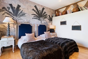 Een slaapkamer met een groot bed, twee nachtkastjes, een wandplank met boeken en een decoratief muurschildering.