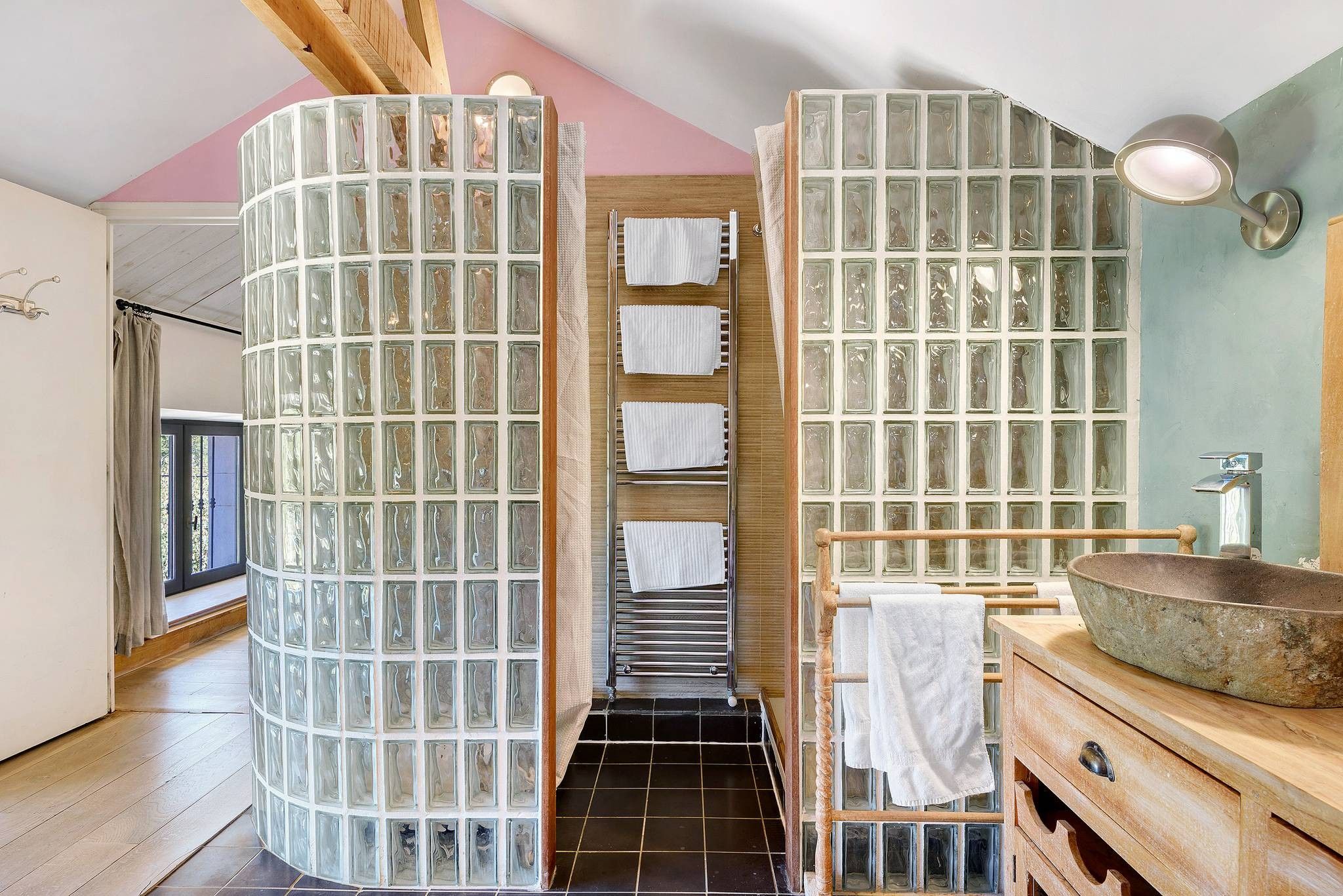Une salle de bain avec un mur en blocs de verre, un meuble-lavabo en bois et un sol carrelé de noir.