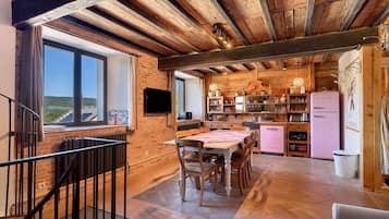 Une cuisine rustique avec des poutres apparentes, un coin repas avec une table et des chaises, et une vue par la fenêtre.