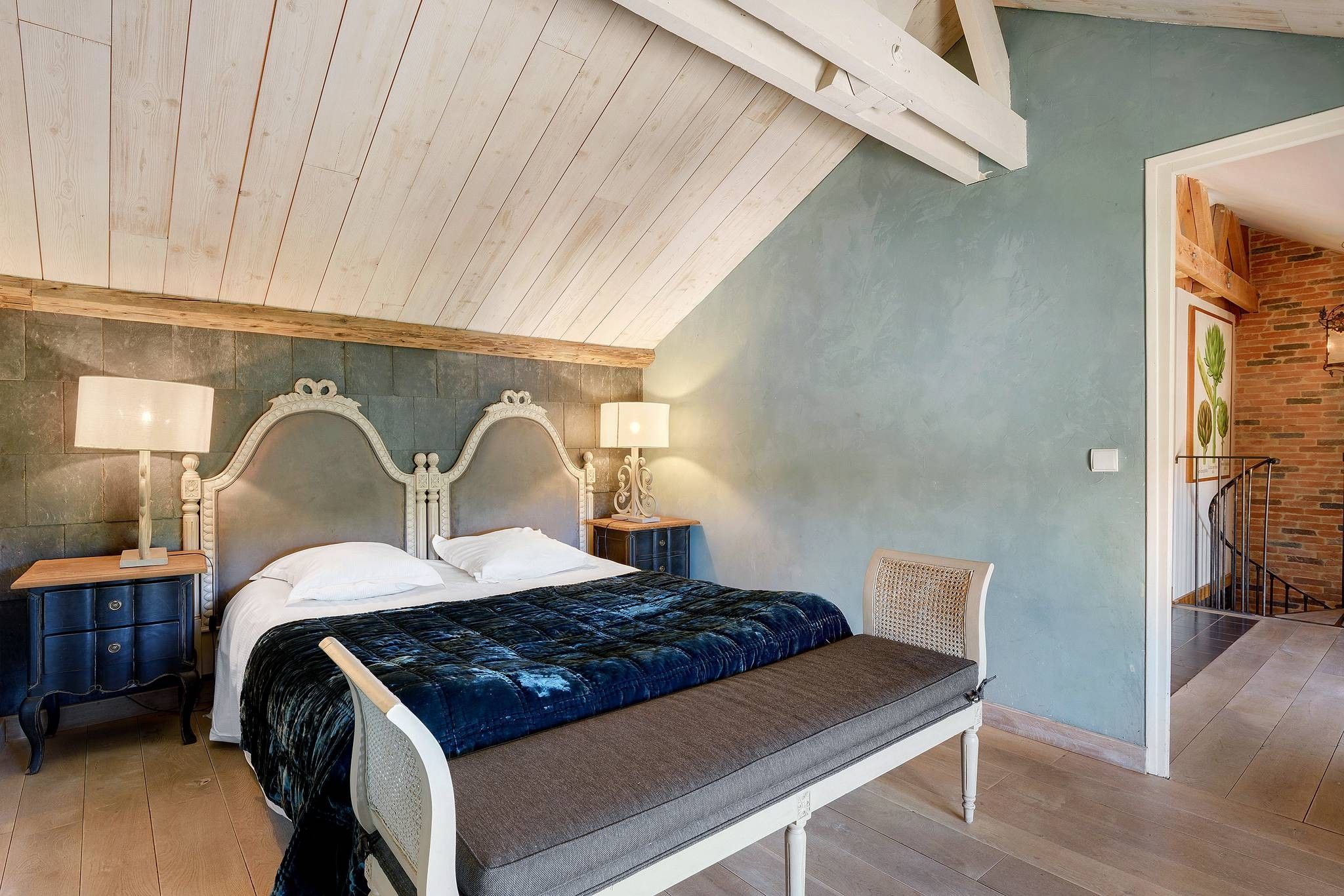 Un dormitorio con una cama, dos mesitas de noche, un banco y una lámpara.