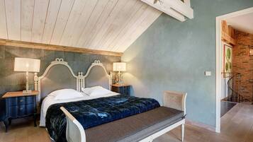 Un dormitorio con una cama, dos mesitas de noche, un banco y una lámpara.
