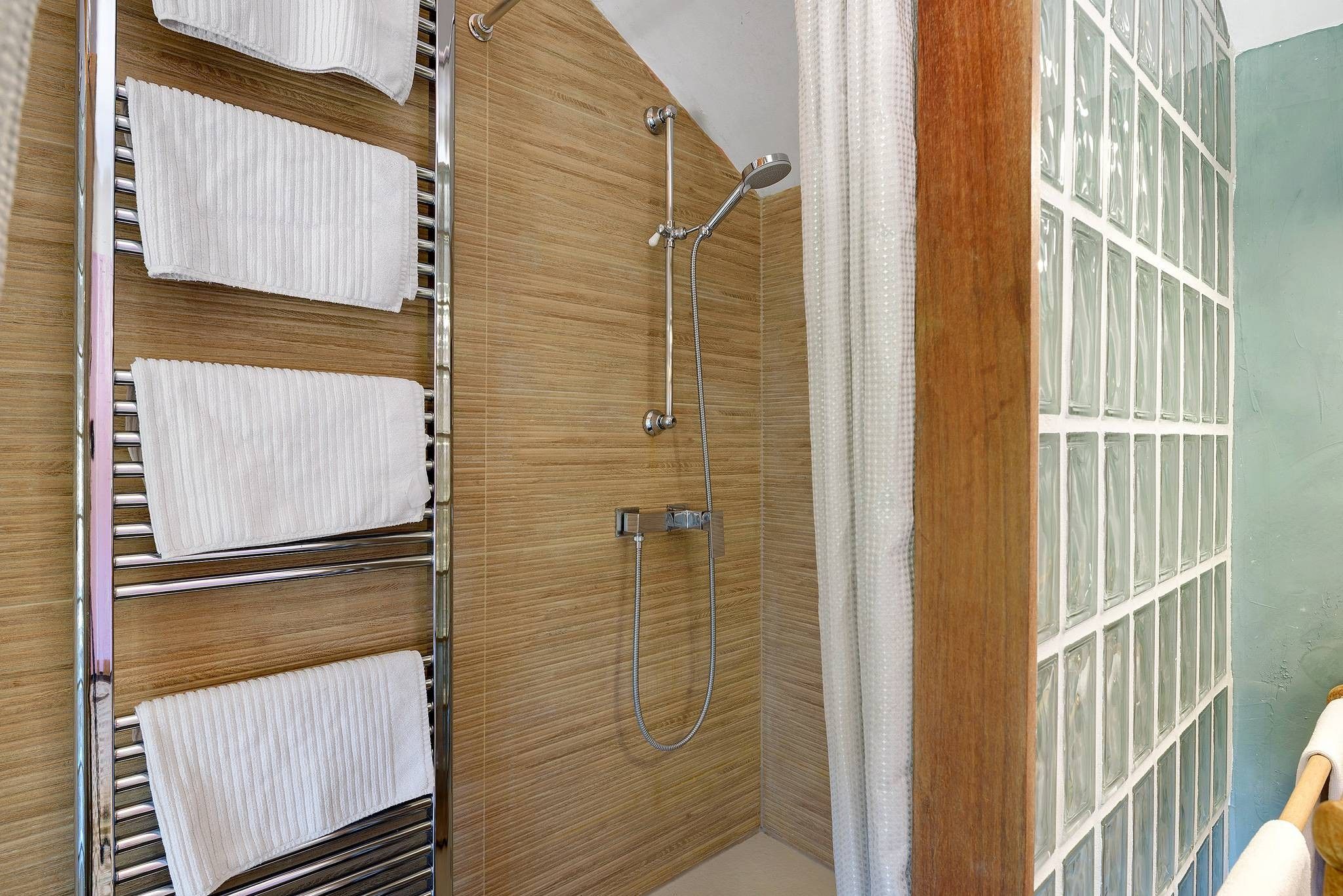 Un baño con ducha, un perchero con varias toallas y una pared de madera.