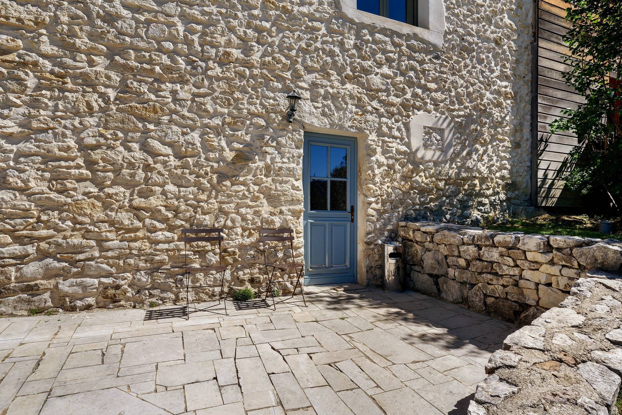 A stone building with a blue door, a bench, and a small garden area.
