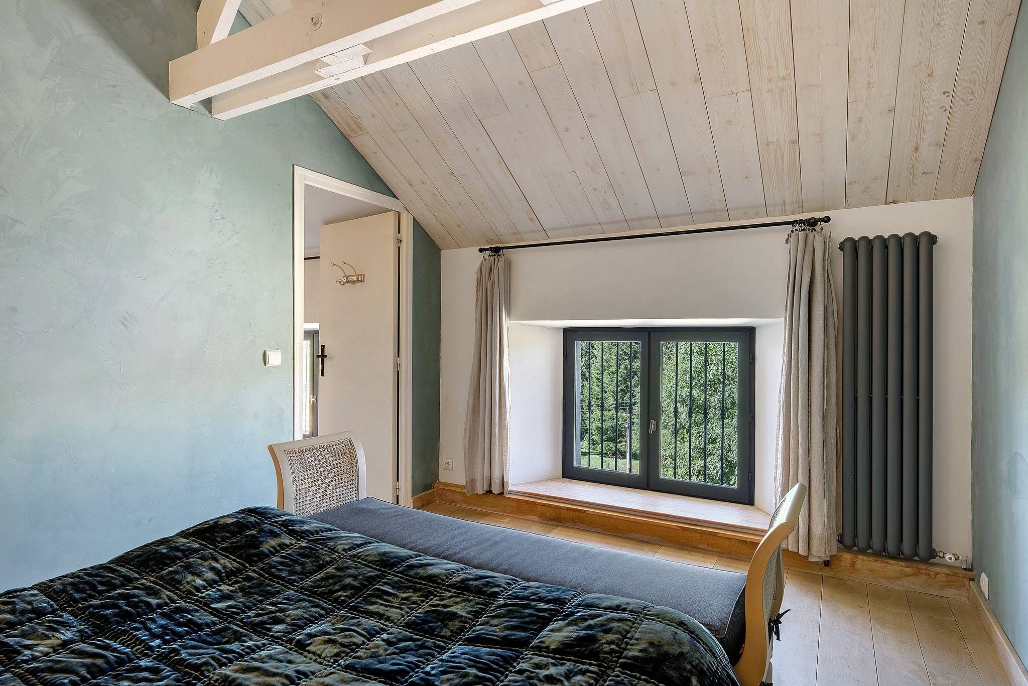 Un dormitorio con cama, ventana, sillón y radiador.