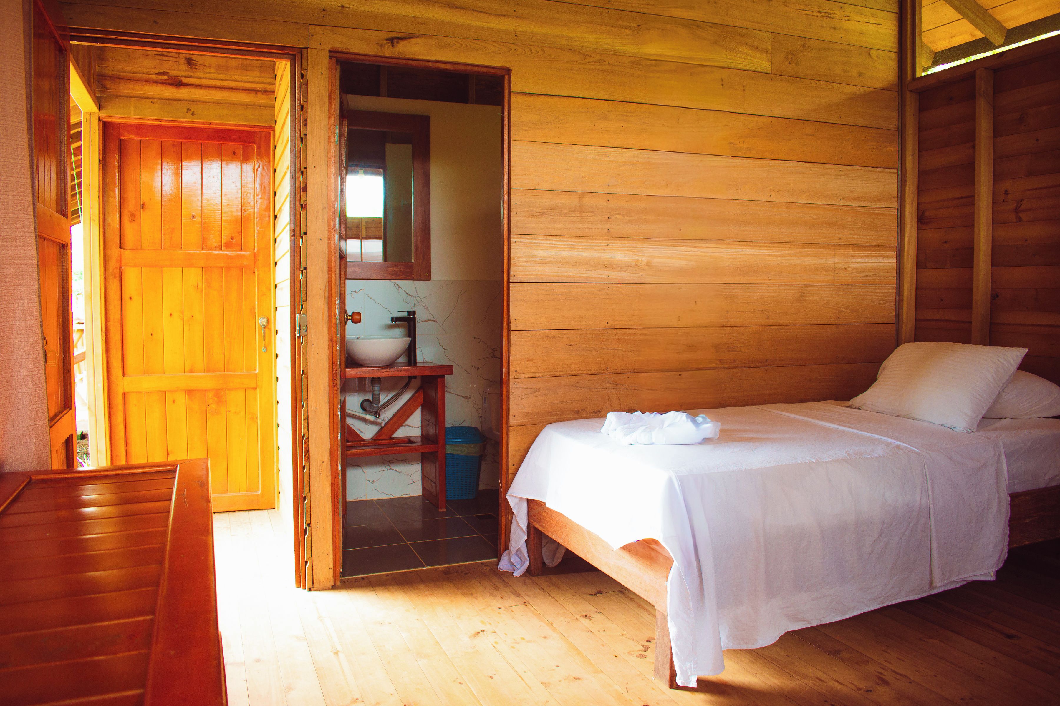 Une pièce de cabane en bois comprenant un lit, une petite table et une salle de bain avec un miroir et un lavabo.