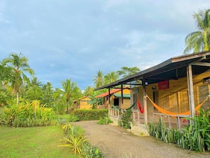 A bungalow with a porch, surrounded by lush greenery and palm trees.