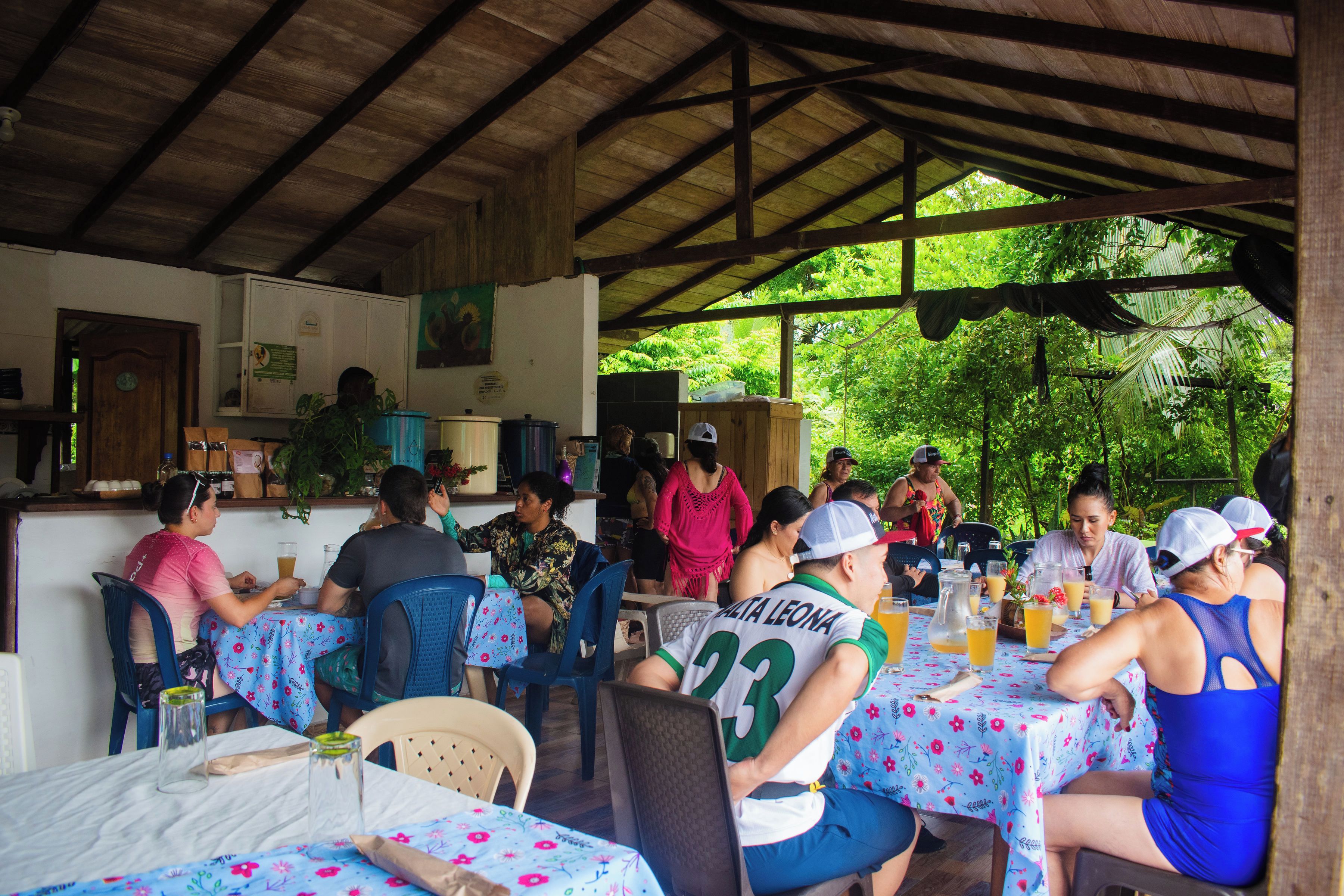 An outdoor dining area with tables covered in floral tablecloths, surrounded by greenery.