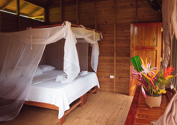 A wooden room with a four-poster bed, a wooden door, and a potted plant with flowers.