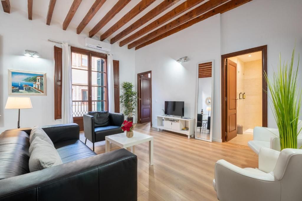 Amplia sala de estar con un sofá de cuero negro, una mesa de centro blanca y un televisor. Cuenta con techo de madera y una puerta que da a un baño.