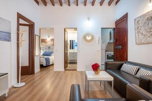 A modern living room with a sofa, a coffee table, and a bench. There is a door leading to a bedroom with a bed and a bathroom with a mirror and a sink. - Holiday Palma Apartments (Palma)