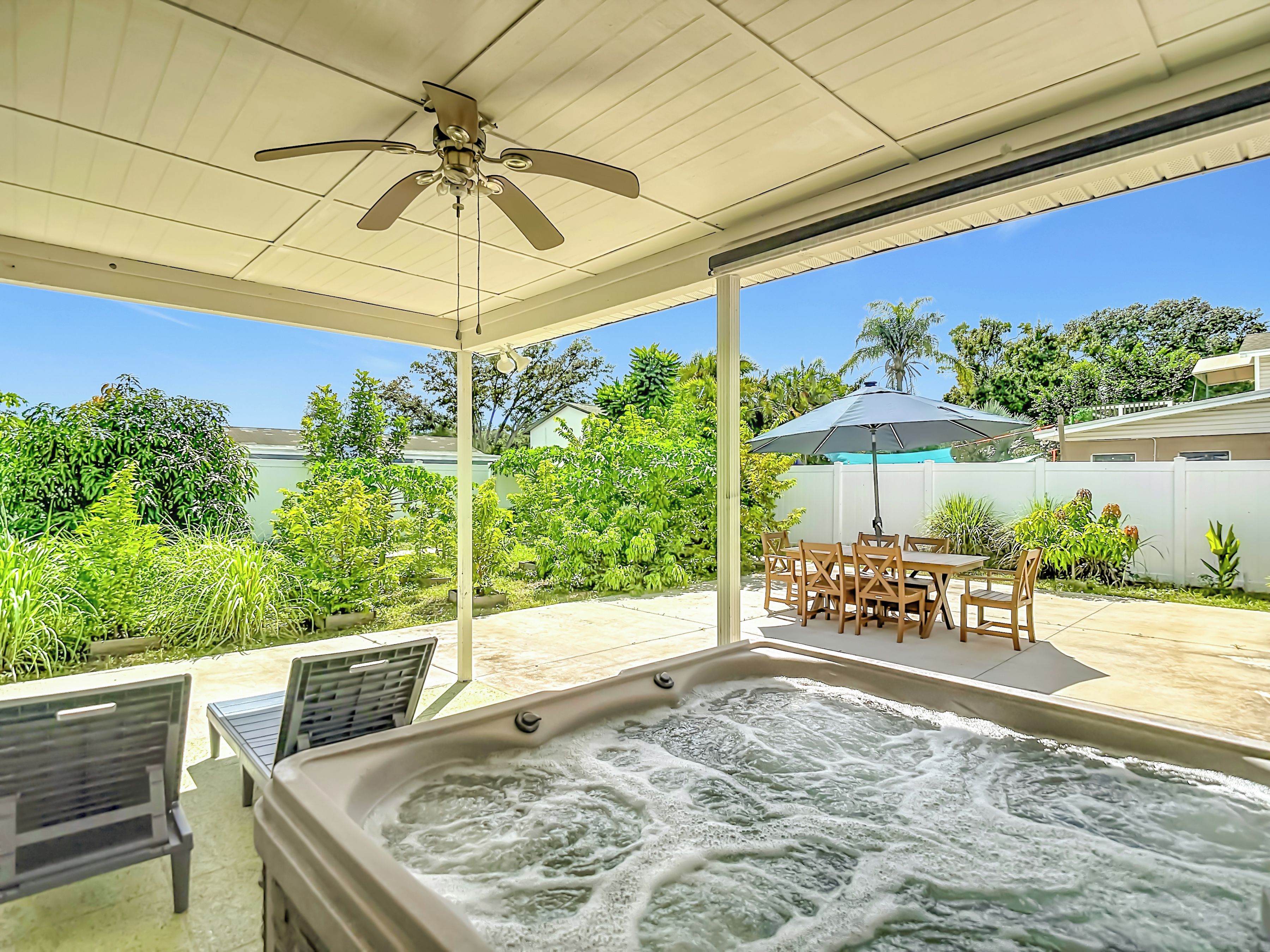 A covered outdoor area with a hot tub, patio furniture, and a ceiling fan.