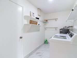 A laundry room with a washing machine, a drying rack, and a shelf with a laundry sign. - Charming Tampa retreat with a private hot tub (Tampa)