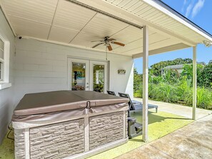 Ein überdachter Außenbereich mit Whirlpool, Deckenventilator und Blick auf einen Garten.