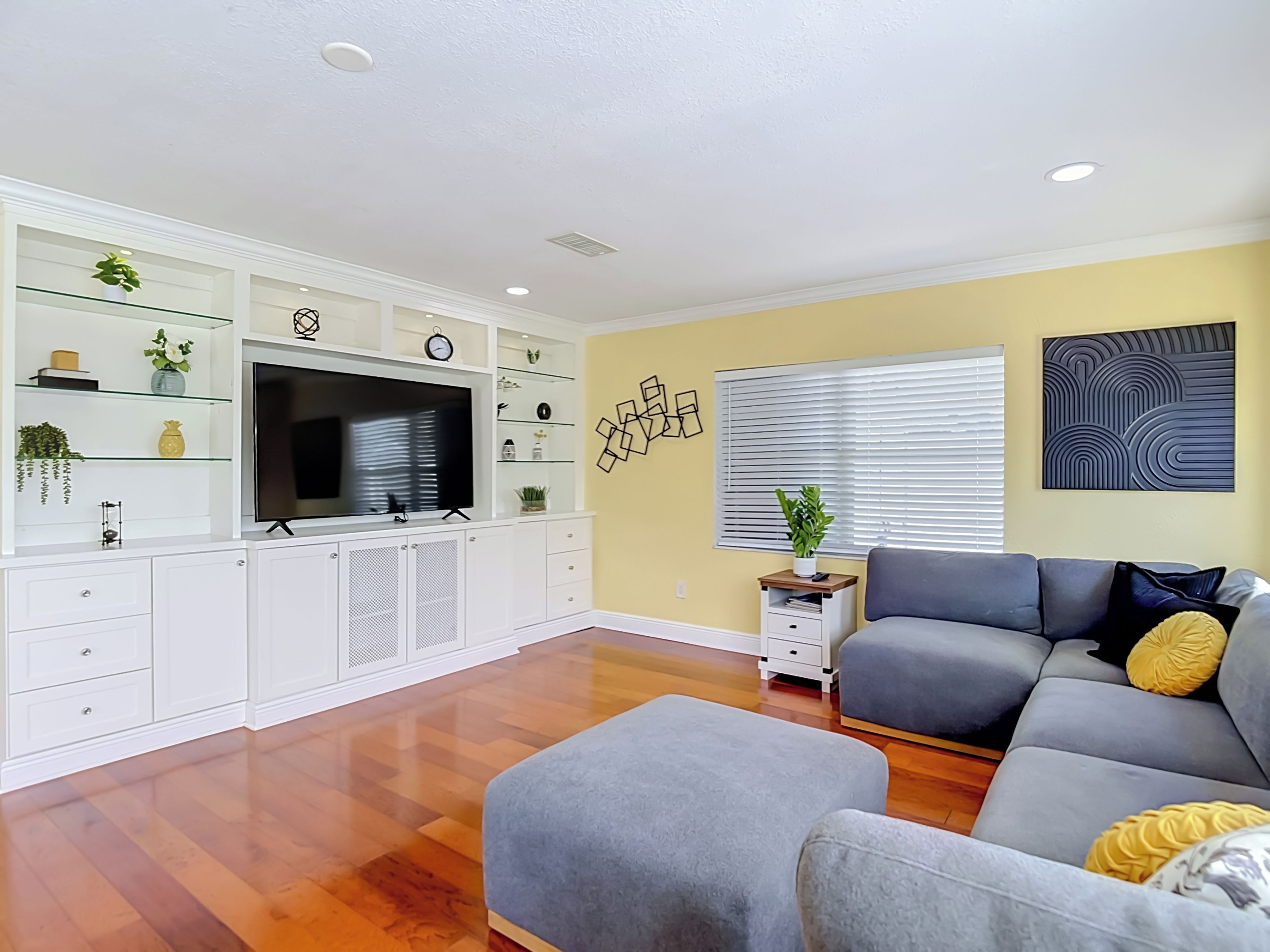 A living room with a grey sofa, a flat-screen TV, white cabinetry, and a wooden floor. - Charming Tampa retreat with a private hot tub (Tampa)