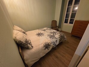 Ein Schlafzimmer mit einem Bett, einer Holzkommode, einem Stuhl und einem Fenster mit Vorhängen.