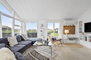 A spacious living room with a sofa, coffee table, and a chair. There is a television on the wall and a bookshelf filled with books and decorative items. - LK2285 Løkken - Hybenvej 33 (Nr. Lyngby)