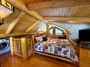 Un dormitorio acogedor en el ático con una cama de madera, una lavadora y un televisor.