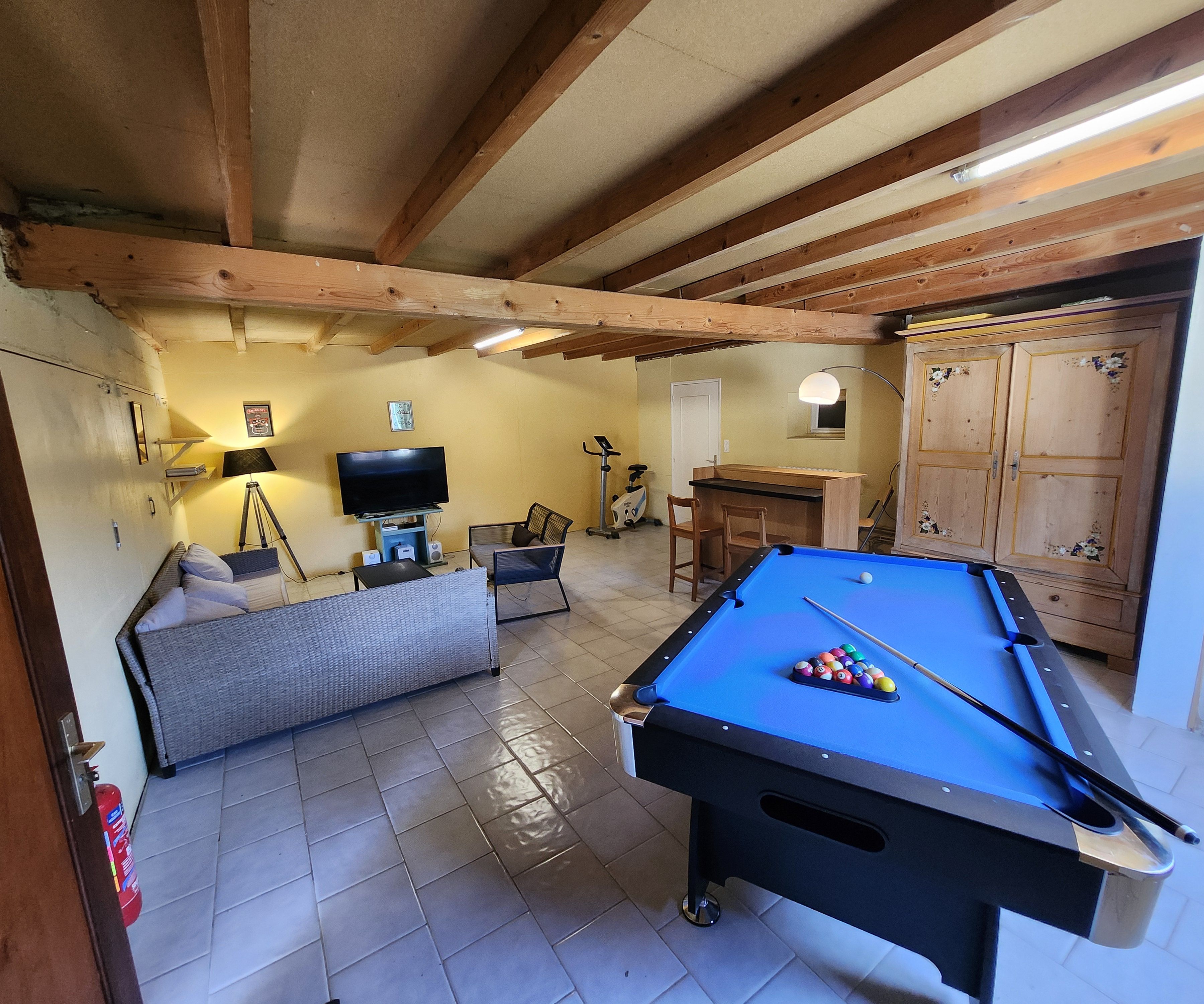 Una mesa de billar con bolas, un sofá, un televisor y un armario en una habitación con vigas de madera.