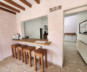 A kitchen with a wooden countertop, bar stools, and a tiled floor.