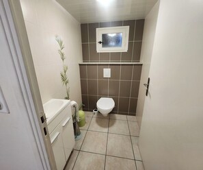 Een kleine badkamer met toilet, wastafel en een raam boven het toilet.