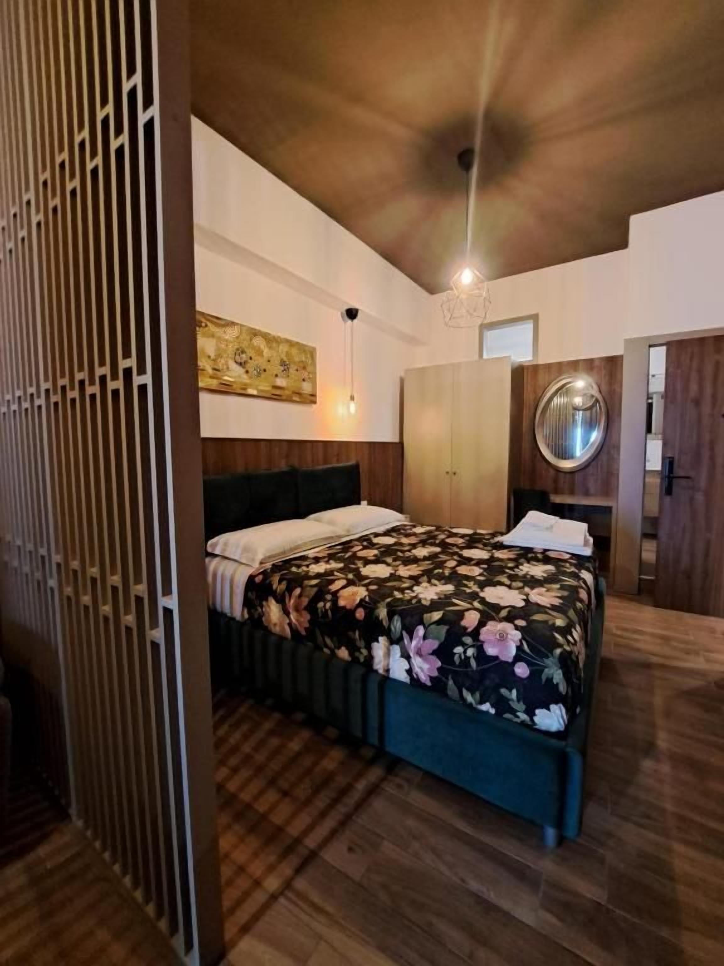 Un dormitorio con cama, cabecera de madera, una obra de arte en la pared y un espejo circular.