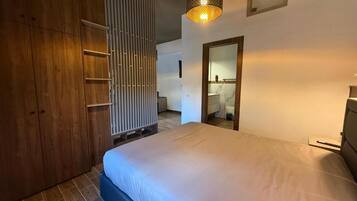 Un dormitorio con cama, armario, espejo y lámpara colgante.