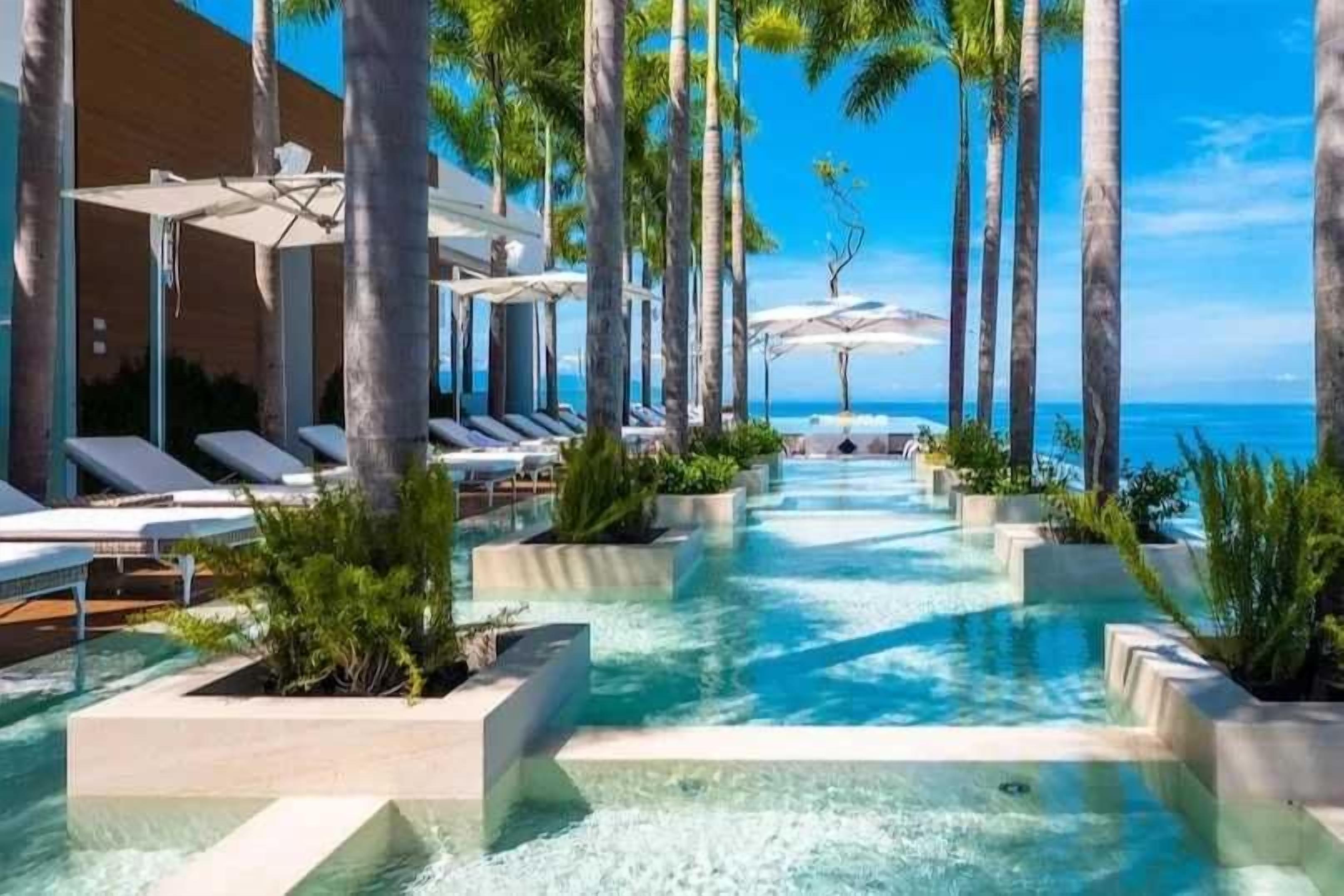A pool area with lounge chairs and umbrellas, surrounded by palm trees.