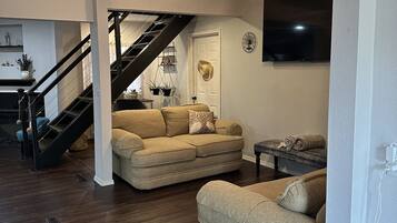 A living room with a sofa, a coffee table, a dining table, and a staircase leading to another level.