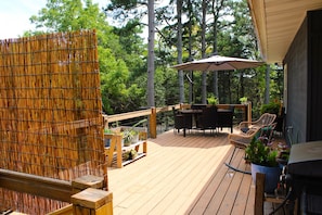 Une terrasse en bois, meublée pour l’extérieur, avec un barbecue et des plantes en pot.