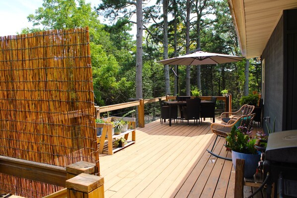 Una terraza de madera con mobiliario exterior, una parrilla y plantas en macetas.