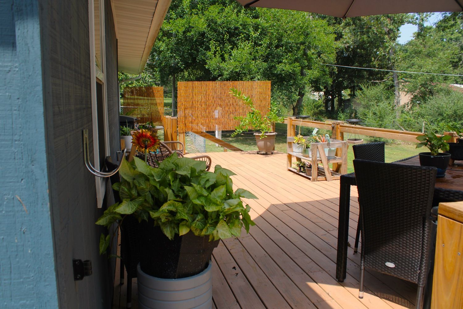 Une terrasse en bois, agrémentée de meubles d’extérieur, de plantes en pot et d’une clôture en bois.