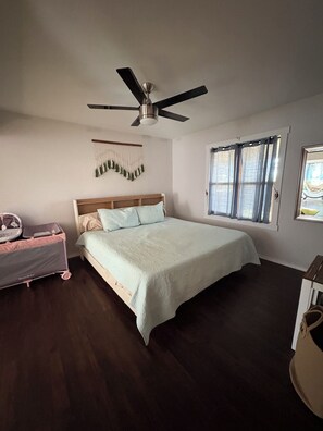 Un dormitorio con cama, ventilador de techo, ventana con cortinas y un adorno en la pared.