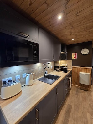 A modern kitchen with a wooden ceiling, a microwave, a sink, and a toaster.