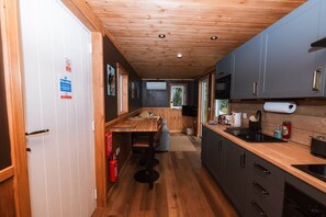 A compact kitchen with wooden cabinets, a dining area with stools, and a visible fire extinguisher.