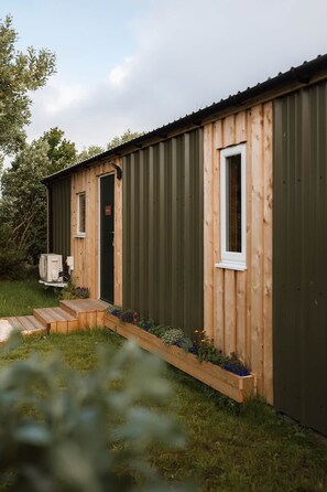 Una pequeña estructura de madera con revestimiento de metal verde, una puerta y una ventana.