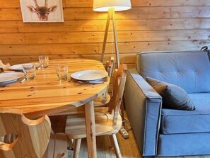 A wooden dining table with plates and glasses, a blue sofa, and a lamp. - 50m from ski slopes, 1st floor, balcony, tv, ski locker, 24m², Risoul (Risoul)