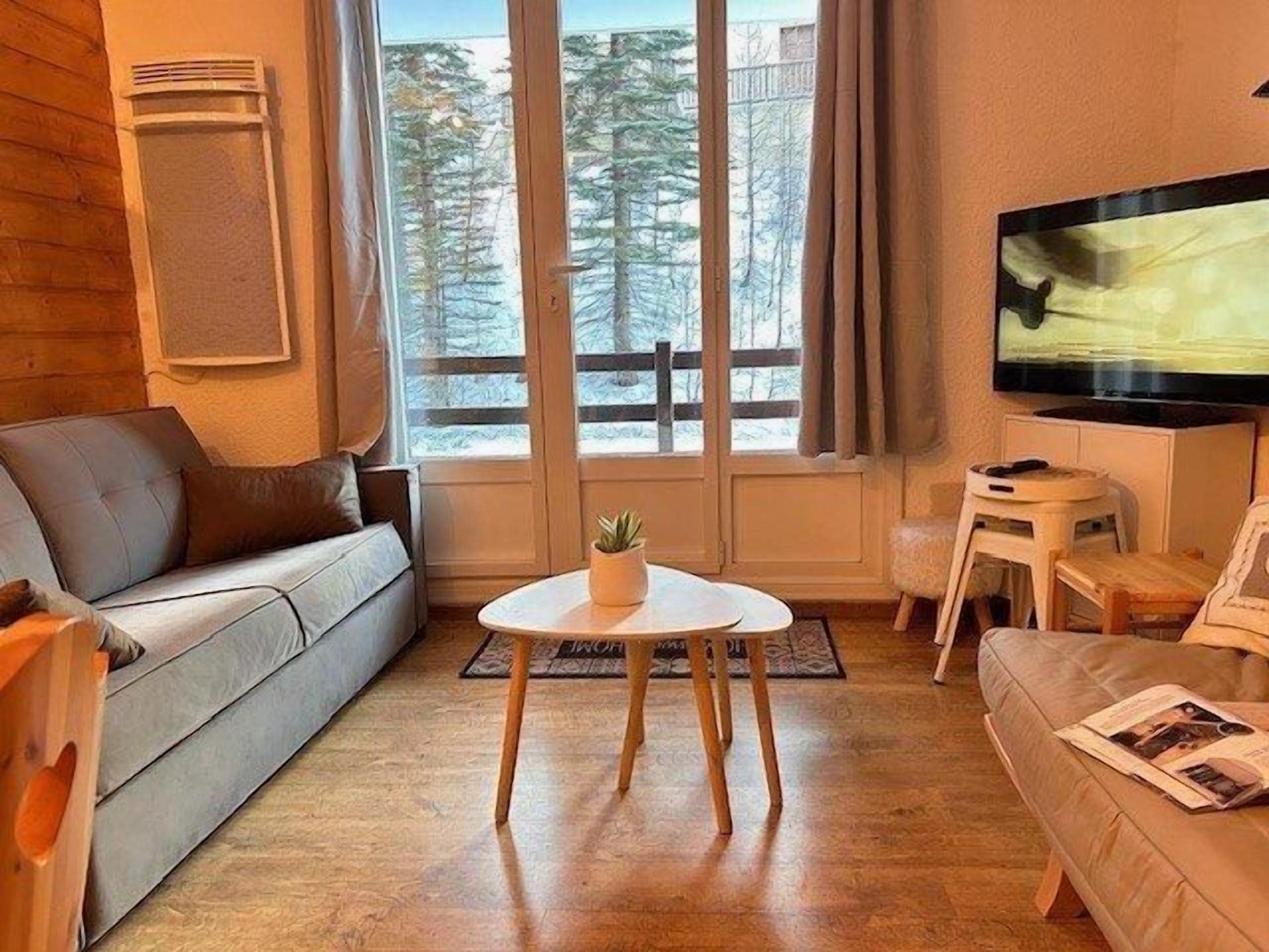 Un salon chaleureux avec un canapé, une petite table sur laquelle est posée une plante, et un téléviseur fixé au mur.