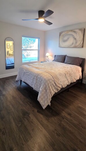 Une chambre à coucher avec un lit, un ventilateur de plafond, une fenêtre donnant sur un beau paysage et un tableau accroché au mur.