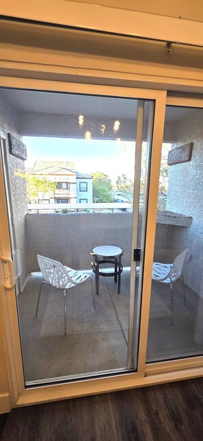 Une porte-fenêtre coulissante donnant sur un balcon équipé de deux chaises et d’une petite table.