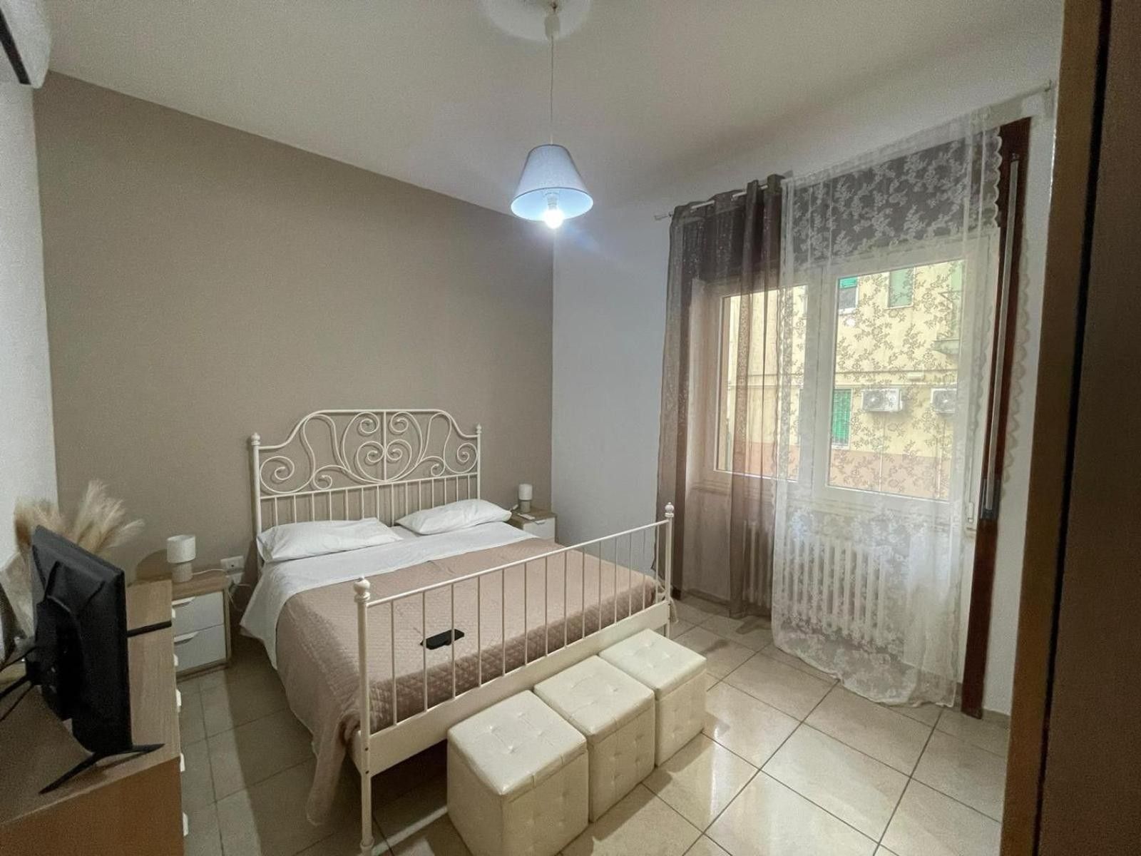 Un dormitorio con cama, mesita de noche, lámpara y ventana con cortinas.