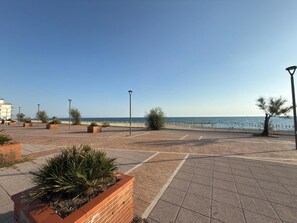 Un passeig pavimentat amb vista despejada al mar, fanals i un edifici al fons.