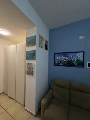 Une pièce avec un canapé beige, une armoire blanche et un mur bleu orné de plusieurs tableaux.